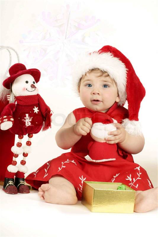 A beautiful nine month old baby girl in a red dress and santa hat playing with christmas ...