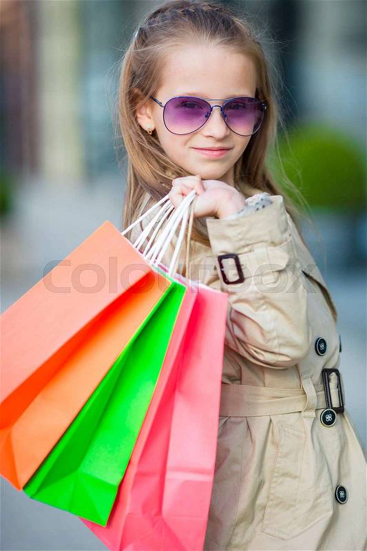 Portrait of adorable little girl with shopping bags outdoors. Fashion toddler kid in european city outdoors, stock photo