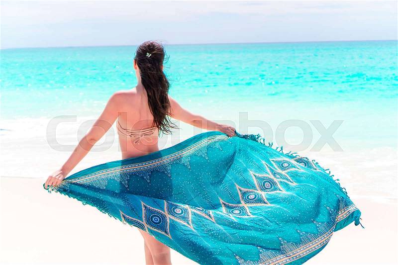 Beautiful bikini body woman relaxing in flowing cover-up beachwear fashion wrap on ocean sunset background, stock photo