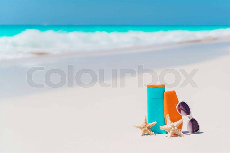 Beach accessories needed for sun protection. Suncream bottles, goggles, starfish on white sand beach background ocean, stock photo
