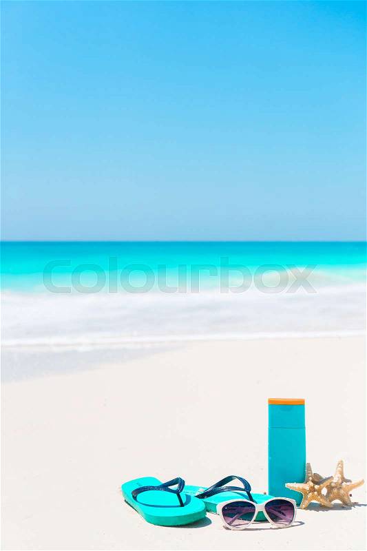 Beach accessories needed for sun protection. Suncream bottles, goggles, flip flops, starfish on white sand beach background ocean, stock photo