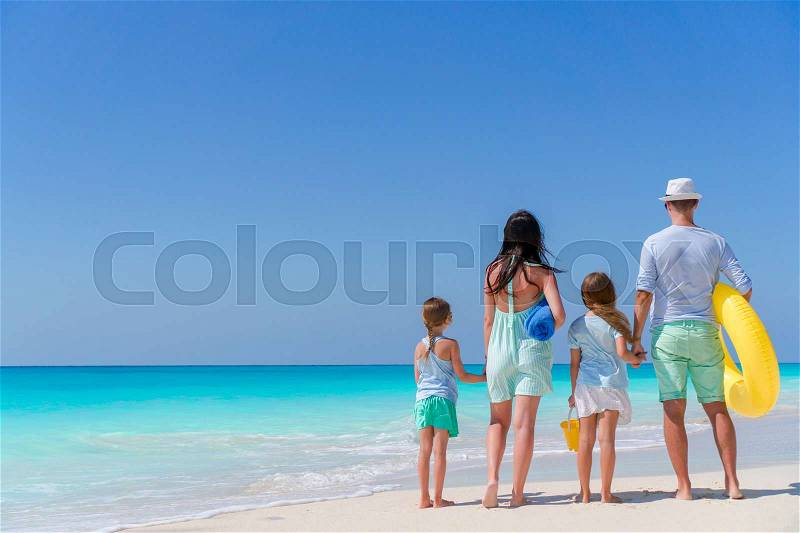 Back view of family of four on the beach. Family travel concept, stock photo