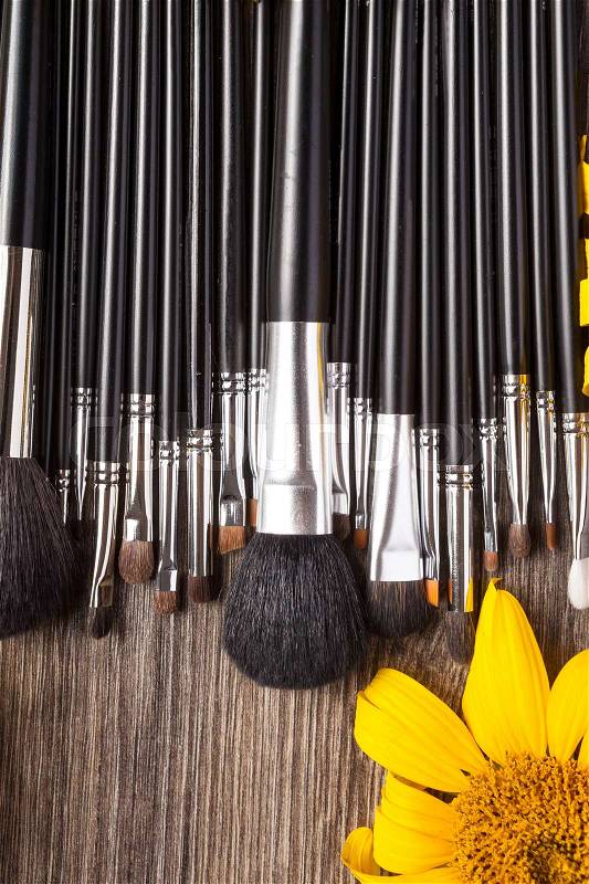 Make up brushes next to flowers on wooden background, stock photo