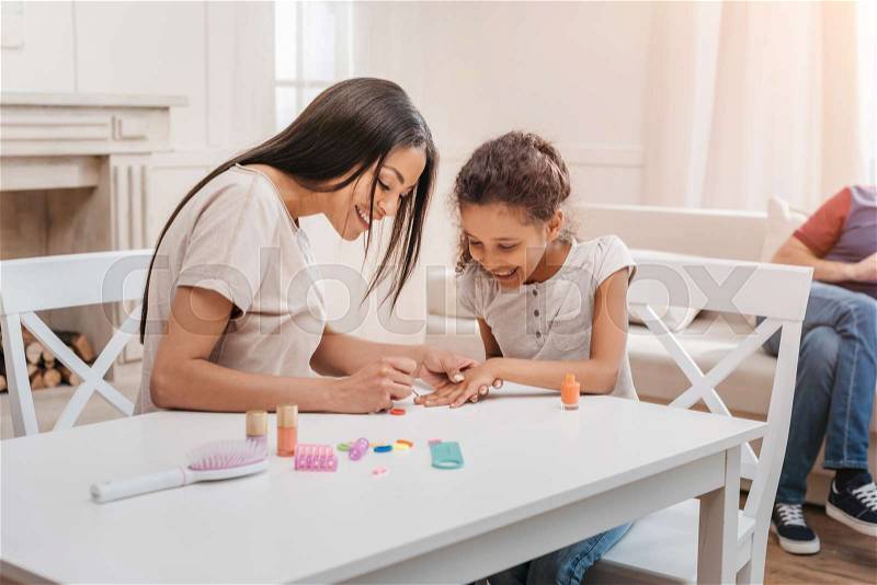 Happy african american mother and daughter doing manicure at home, stock photo