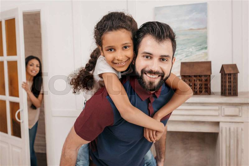Happy father piggybacking little daughter and smiling at camera at home, stock photo