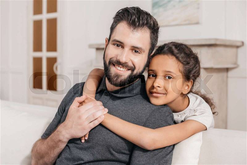 Portrait of little daughter hugging smiling father, multicultural family at home, stock photo