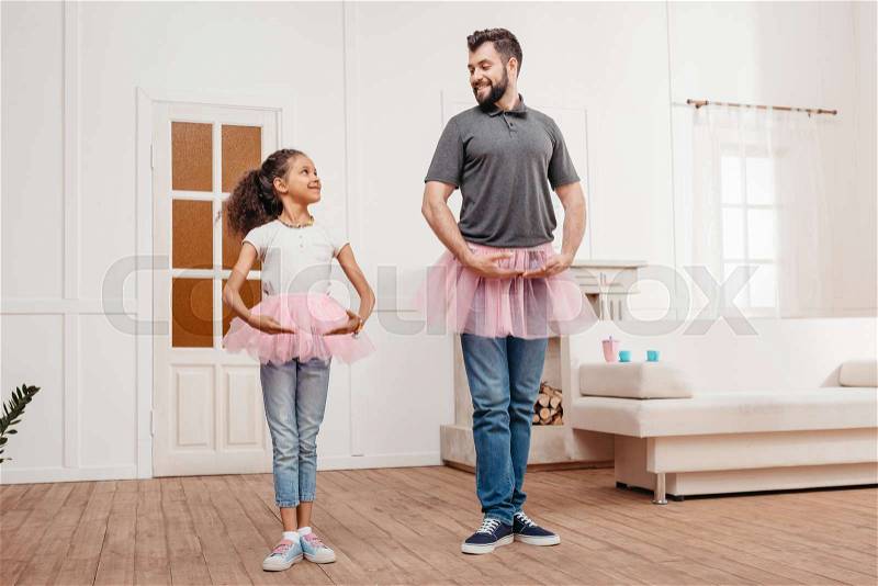 Multicultural family in pink tutu tulle skirts dancing at home, stock photo