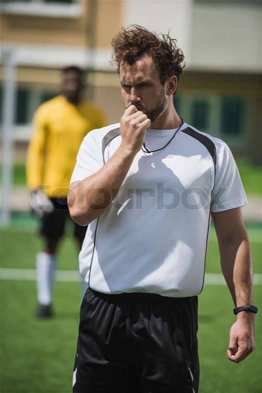 Soccer referee whistling in whistle on soccer pitch during game, stock photo
