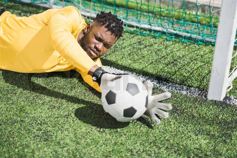 Portrait of african american goalkeeper catching ball during soccer match, stock photo