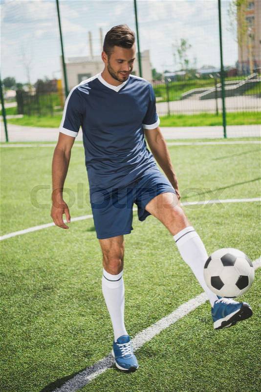 Athletic soccer player training with ball on soccer pitch, stock photo