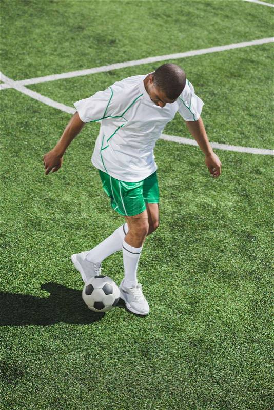 African american soccer player training with ball on soccer pitch, stock photo
