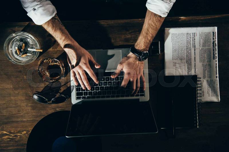 Cropped shot of man using laptop with blank screen while sitting at table with newspaper, ashtray and glass , stock photo