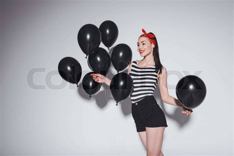 Smiling beautiful pin-up girl posing with black balloons on grey, stock photo