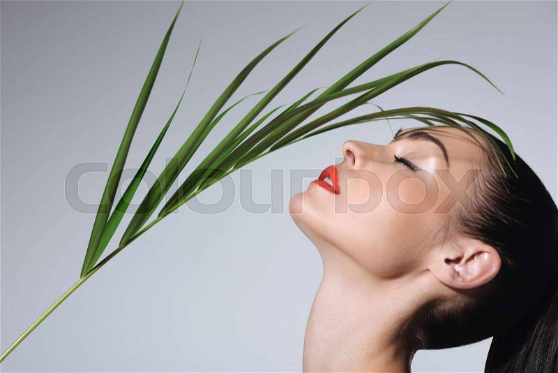Close-up view of beautiful young woman with perfect skin holding green palm leaf , stock photo