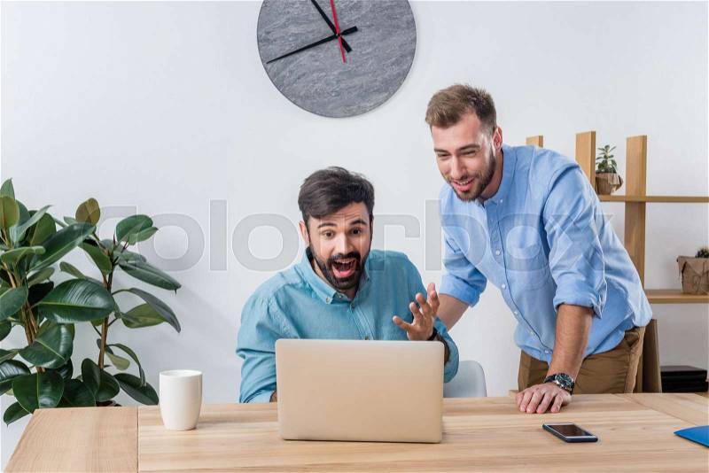 Portrait of excited businessmen looking at laptop screen in office, stock photo