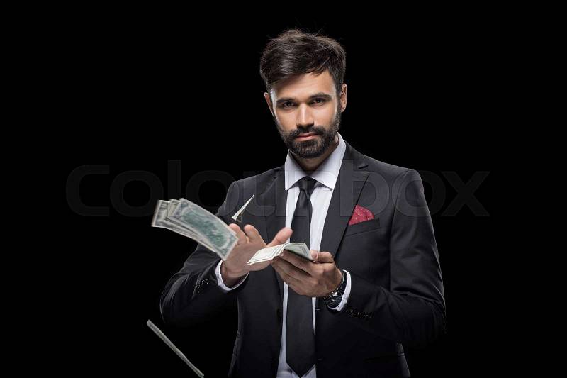 Handsome rich businessman throwing dollar banknotes, isolated on black, stock photo