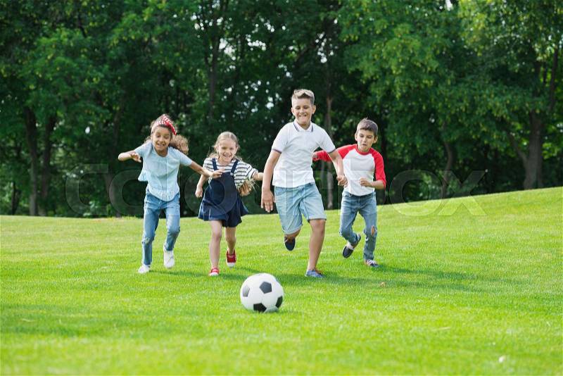 Cute happy multiethnic kids playing soccer with ball in park, stock photo