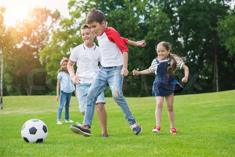 Cute happy multiethnic kids playing soccer with ball in park, stock photo