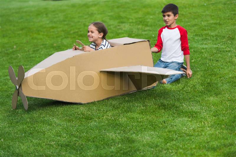 Cheerful little friends playing with toy plane on green lawn in park, stock photo