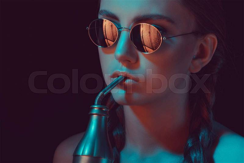 Woman in round sunglasses drinking soda from water bottle with straw, stock photo