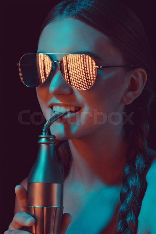 Smiling woman in sunglasses drinking soda from water bottle with straw, stock photo