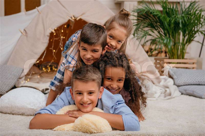 Portrait of happy multiethnic kids lying in pyramid together at home, stock photo
