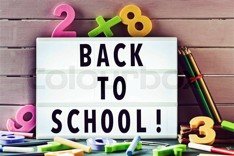 The text back to school in a lightbox placed against a rustic wooden background, surrounded by three-dimensional numbers and chalks and pencil crayons of different colors, stock photo