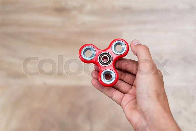 Fidget spinner. Red hand spinner, fidgeting hand toy rotating on child\'s hand. Stress relief. Anti stress and relaxation adhd attention fad boy concept. Free space for text, stock photo
