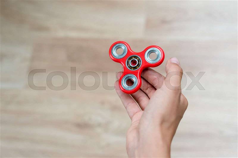Fidget spinner. Red hand spinner, fidgeting hand toy rotating on child\'s hand. Stress relief. Anti stress and relaxation adhd attention fad boy concept. Free space for text, stock photo