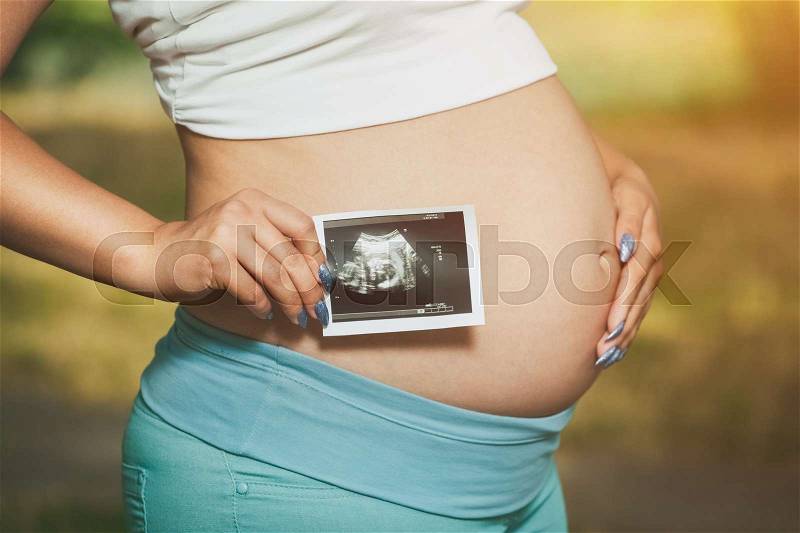 Adult pregnant woman holding a photo Medical ultrasound near the abdomen on a nature background, stock photo