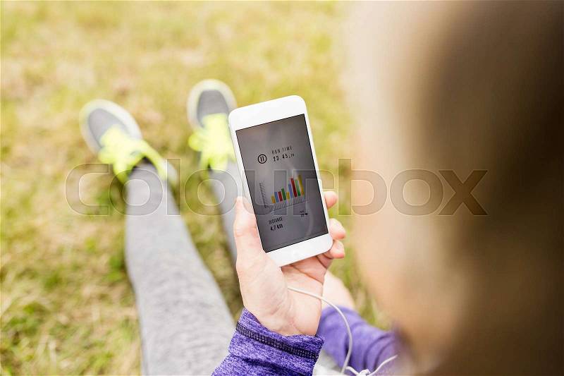 Unrecognizable active senior runner with smart phone outside in nature sitting on the grass using a fitness app for tracking weight loss progress, running goal or summary of her run. Rear view., stock photo