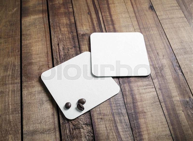 Blank square beer coasters and coffee beans on vintage wooden table background. Responsive design mockup, stock photo