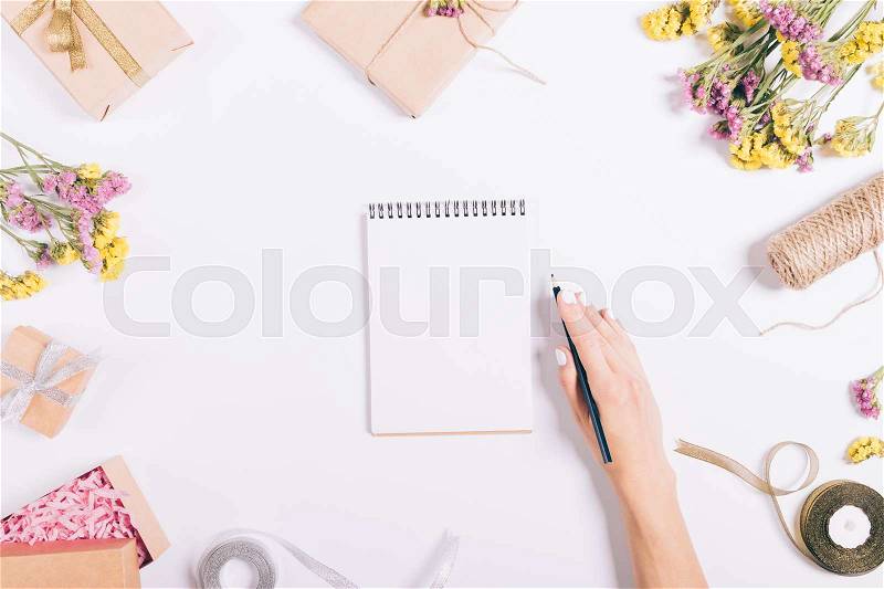 Female hand writing in a paper notebook on a white table with decorations, top view, stock photo