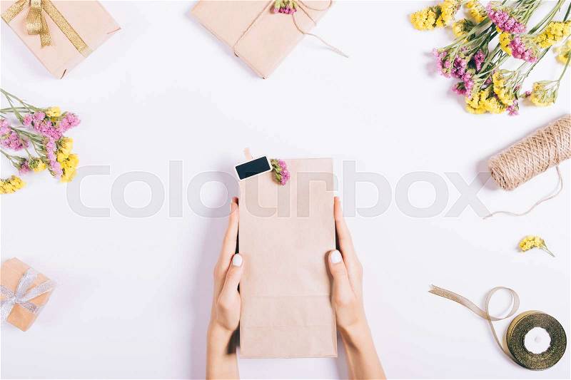 Female hands holding a package with a gift on a white table with decorations, top view, stock photo
