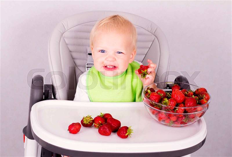 Funny baby boy with a dirty mouth eating strawberry and looking at camera, stock photo