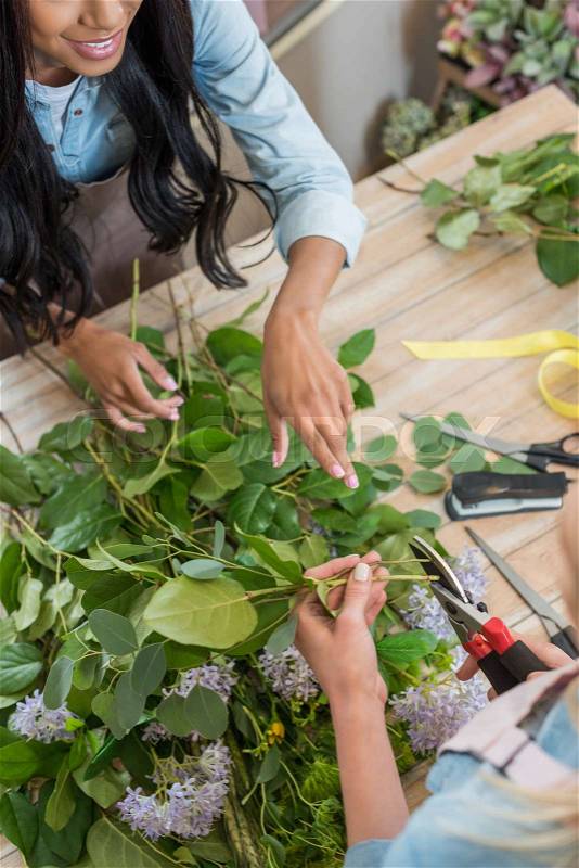 Cropped shot of young florists arranging flowers and cutting plants at workplace, stock photo