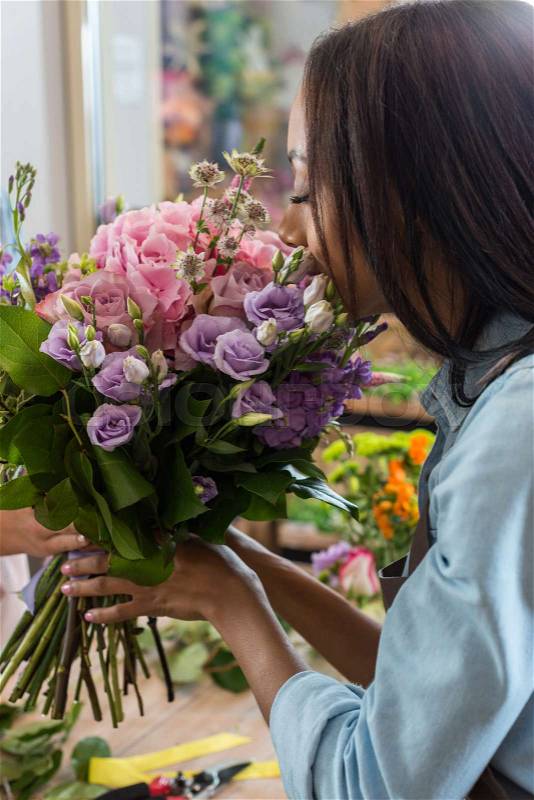 Young african american woman smelling beautiful flowers in flower shop , stock photo