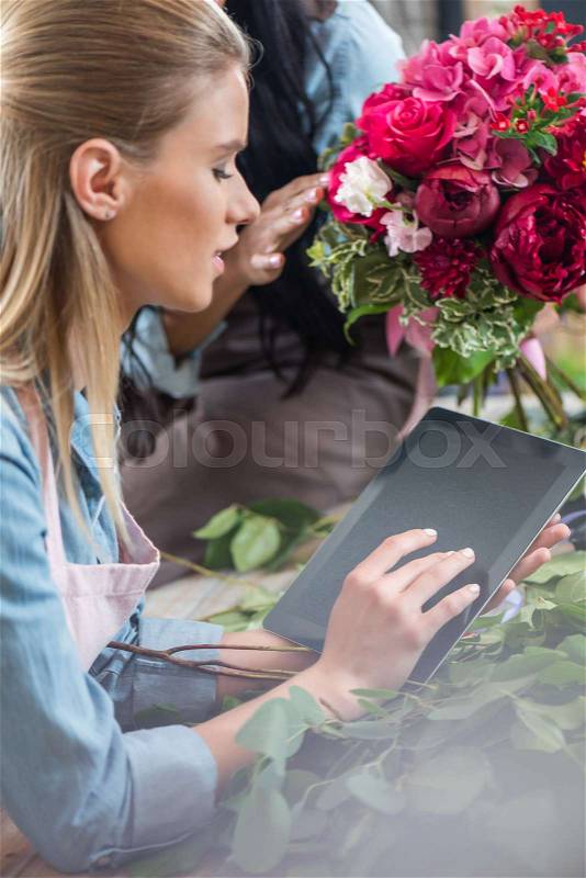 Beautiful young blonde woman using digital tablet with blank screen while working in flower shop, stock photo