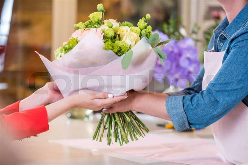 Cropped shot of florist giving beautiful flower bouquet to client, stock photo