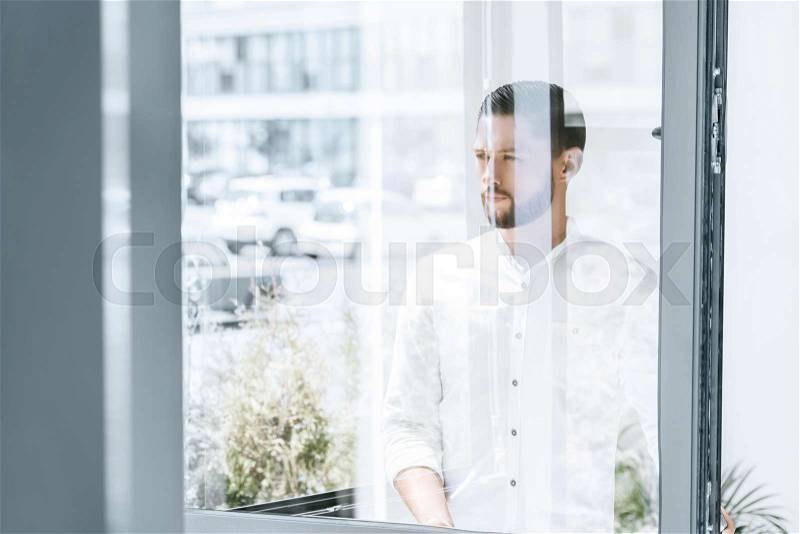 Portrait of pensive caucasian businessman in shirt looking out window, stock photo