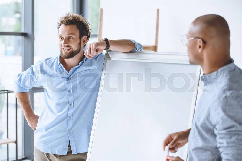 Multiethnic businessmen standing near white board during business presentation, stock photo