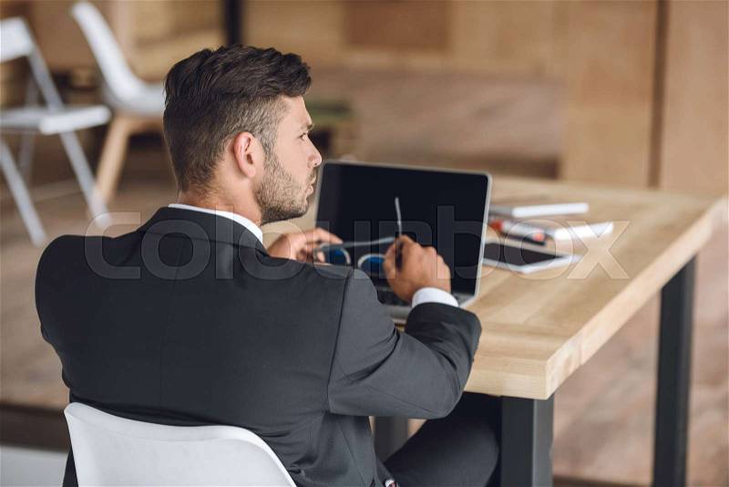 Back view of pensive businessman sitting at workplace with laptop in office, stock photo