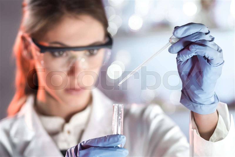 Life scientists researching in laboratory. Focused female life science professional pipetting solution into the glass cuvette. Lens focus on researcher\'s eyes. Healthcare and biotechnology concept, stock photo