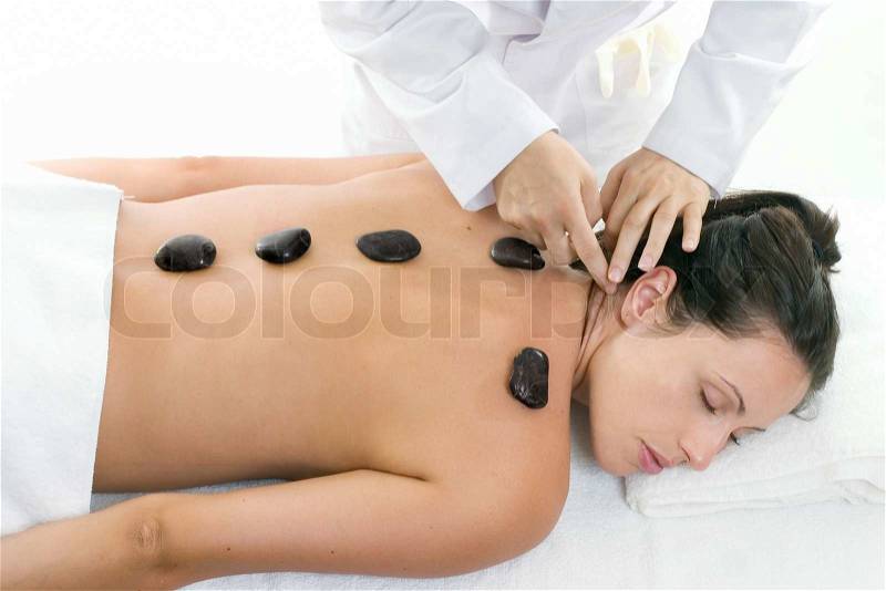 A female receiving massage and hot rock treatment to back and neck at a beauty salon or day spa facility, stock photo