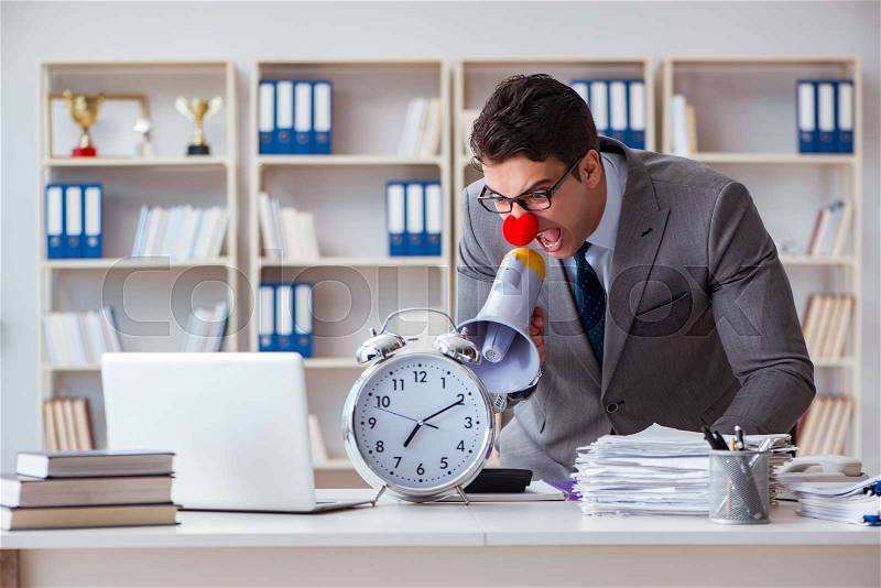Clown businessman in the office angry frustrated with megaphone and alarm clock, stock photo