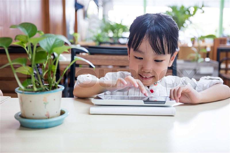 Asian Chinese little girl playing tablet computer at outdoor cafe, stock photo