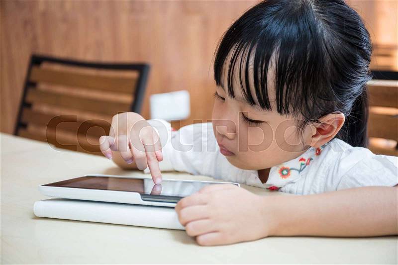 Asian Chinese little girl playing tablet computer at outdoor cafe, stock photo