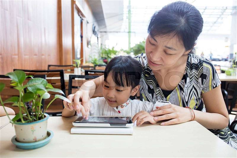 Asian Chinese little girl playing tablet computer with her mother at outdoor cafe, stock photo