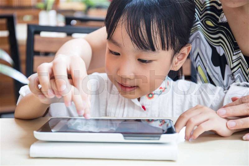 Asian Chinese little girl playing tablet computer with her mother at outdoor cafe, stock photo