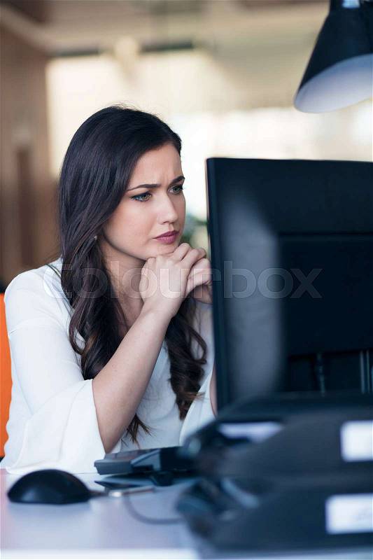 Concentrated middle aged woman working on her computer. Start-up office background, stock photo